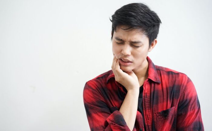 A young man in a plaid shirt holding his jaw in pain on a white background TMJ pain effects of TMJ restorative dentistry dentist in Chesapeake Virginia 